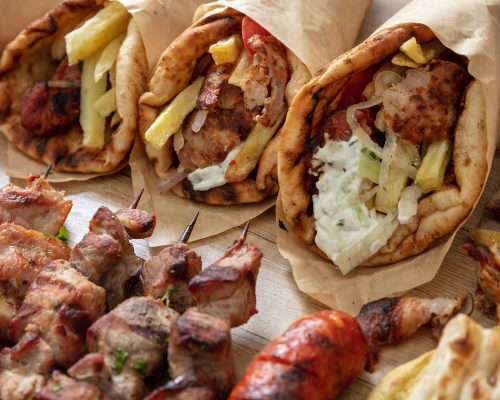 Greek traditional street food, gyro sliced meat, souvlaki skewer. Pita bread, tzatziki yogurt, potato tomato and onion on wooden table, top view